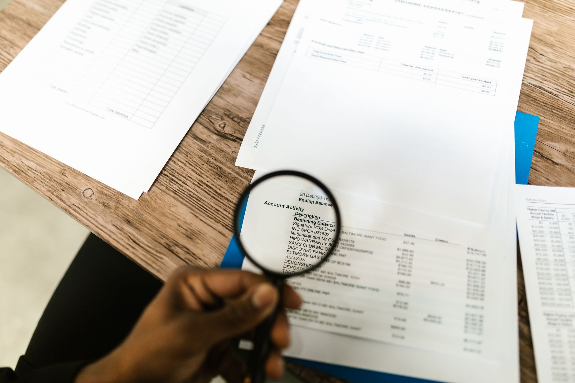 main tenant une loupe au-dessus de documents chiffrés posés sur un bureau en bois
