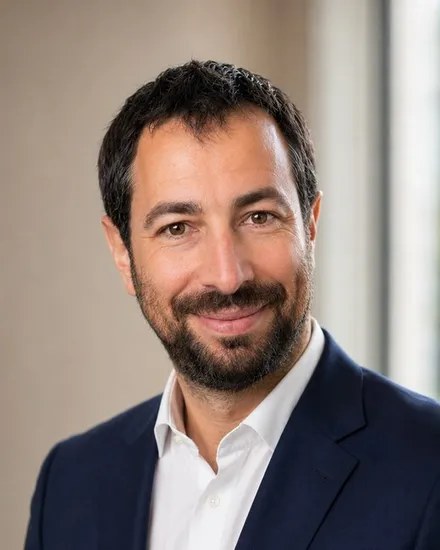 Portrait d'un homme barbu en costume bleu marine et chemise blanche, souriant